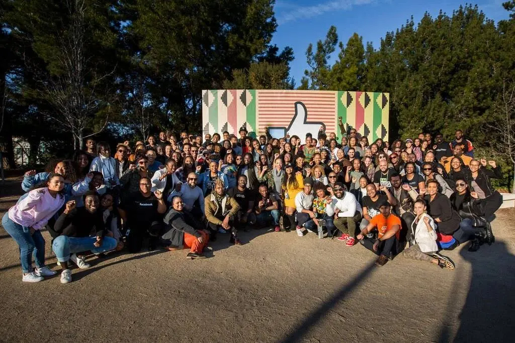 Large group photo of employees posing outdoors in front of a colorful branded backdrop for a Black History Month event, photographed by Marquee Visuals.