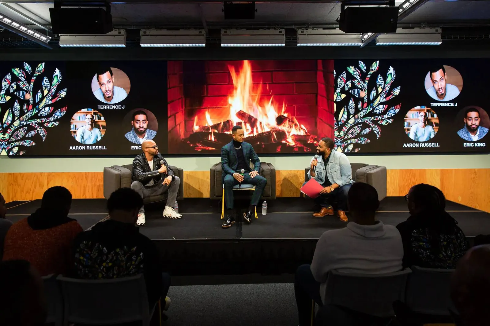 Wide view of a panel discussion with three speakers seated near a fireplace-lit screen at a Black Men at Facebook event, photographed by Marquee Visuals.