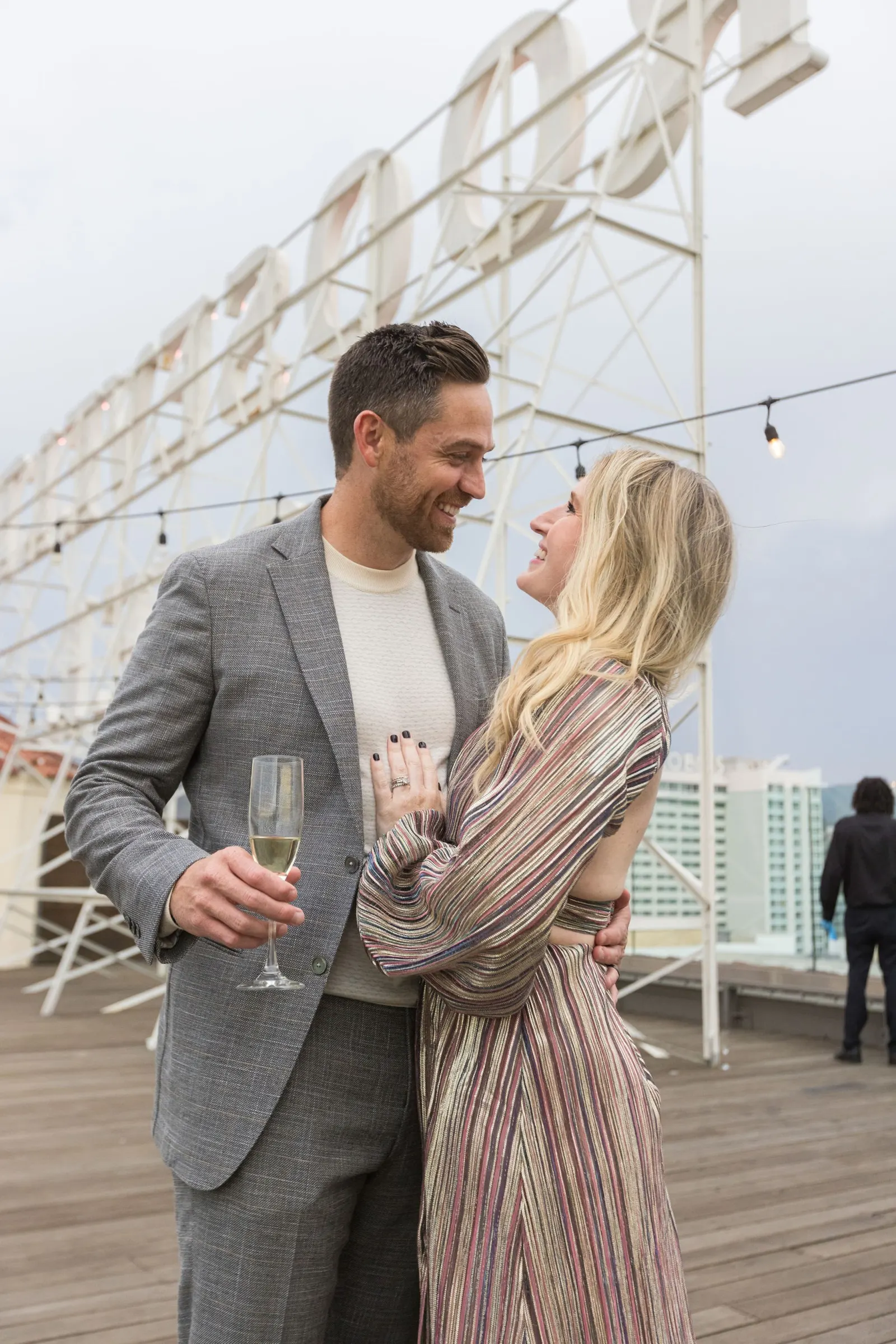 Couple embracing and toasting with champagne on a rooftop at dusk with string lights at the Edge 2025 event, by Marquee Visuals.