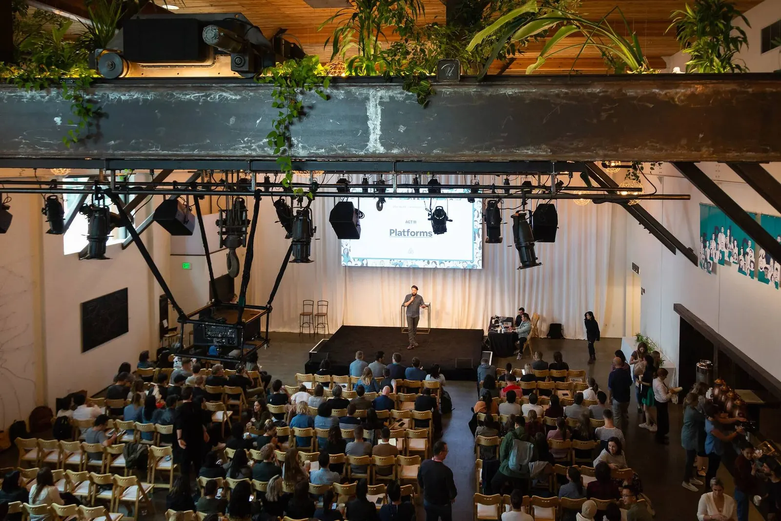 Audience seated in an industrial-style event venue with string lights and greenery during Epic Week, photographed by Marquee Visuals.