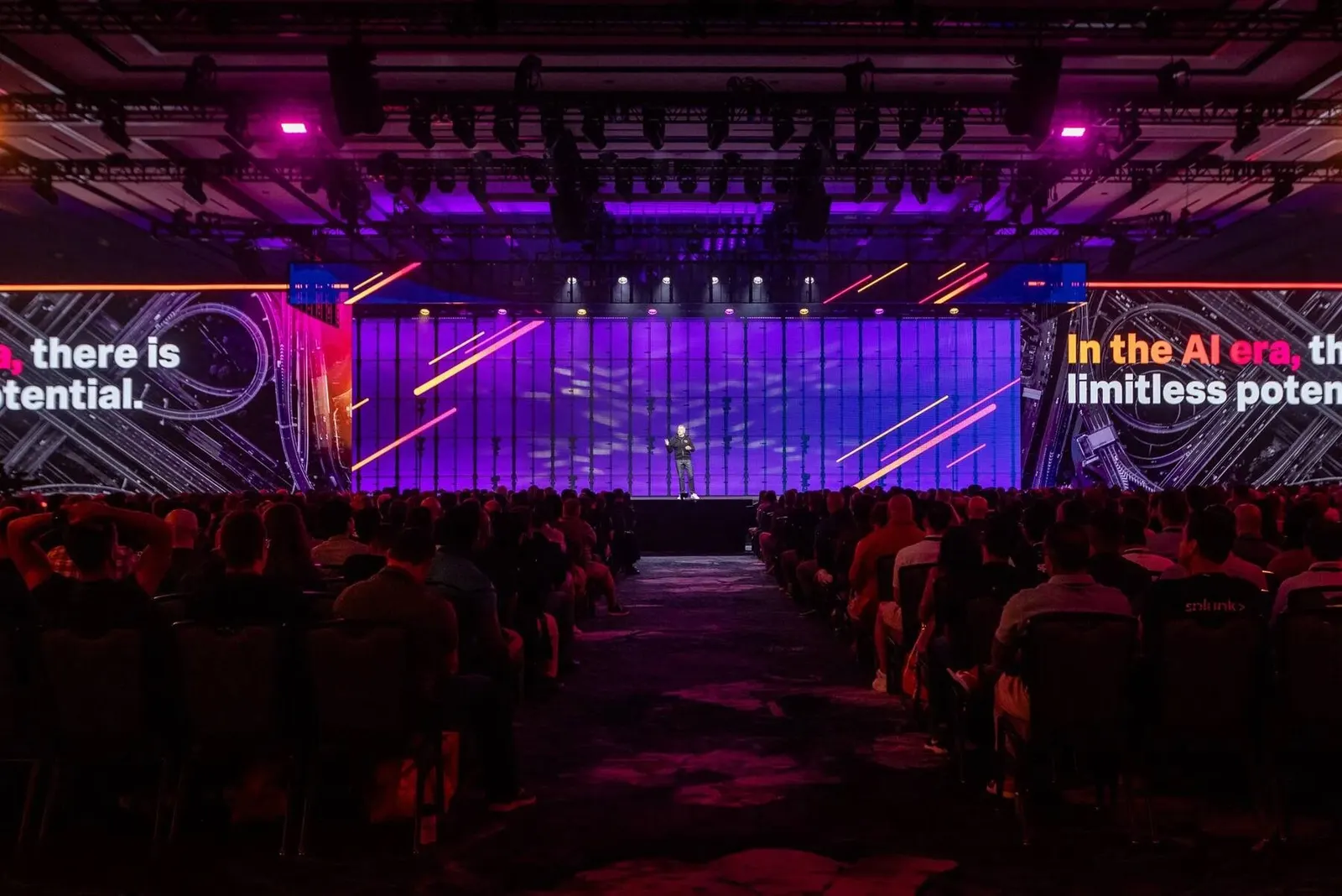 Executive speaker presenting on a dimly lit stage with dramatic red and purple lighting, photographed by Marquee Visuals.