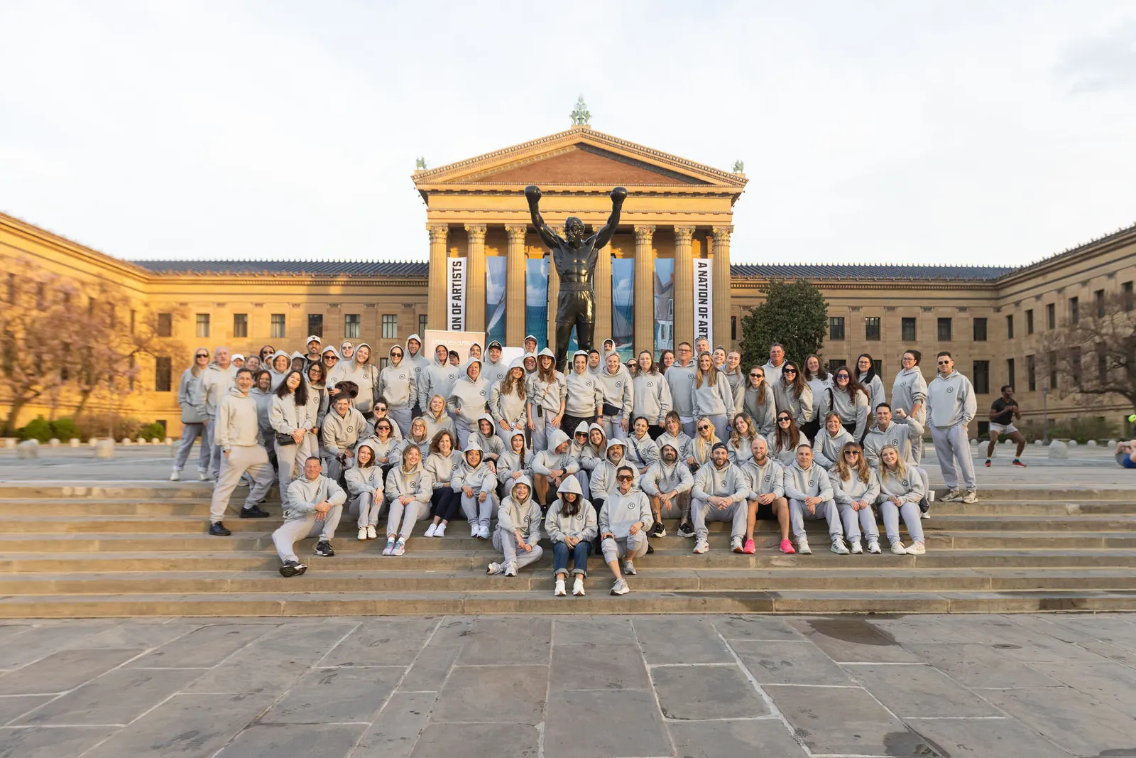 Large group photo of event participants in matching shirts posing on museum steps, photographed by Marquee Visuals.