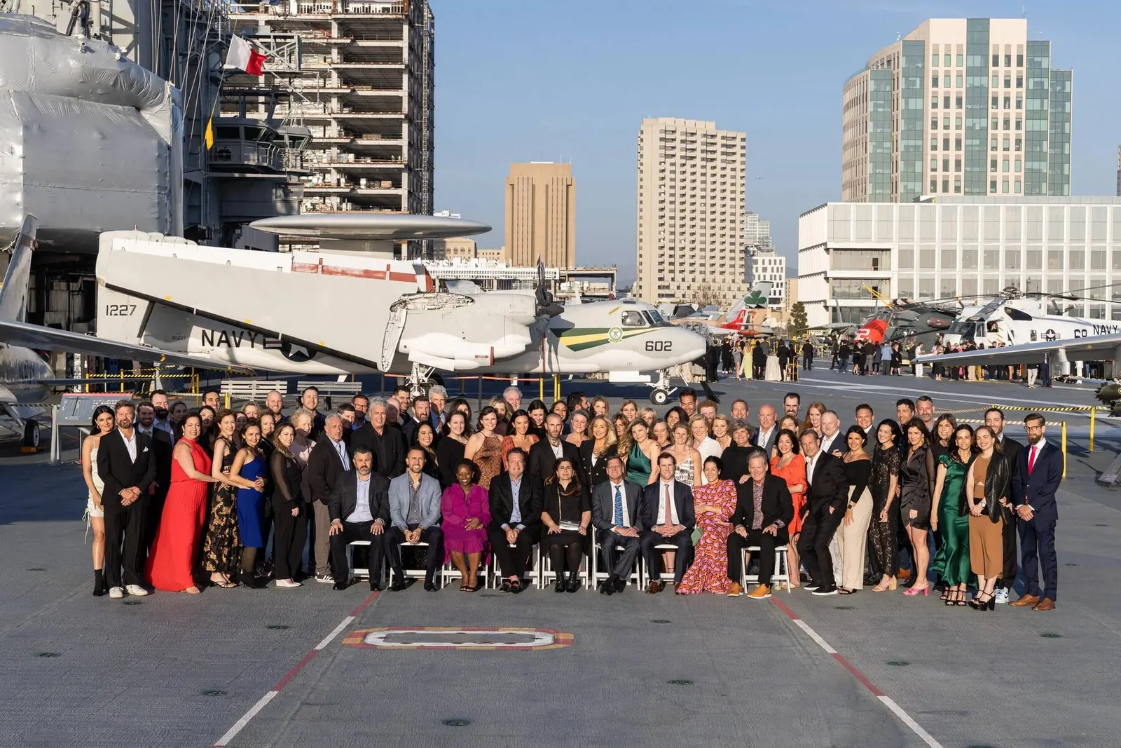 Large formal group photo of attendees posing together on a rooftop deck with a city skyline in the background, photographed by Marquee Visuals.