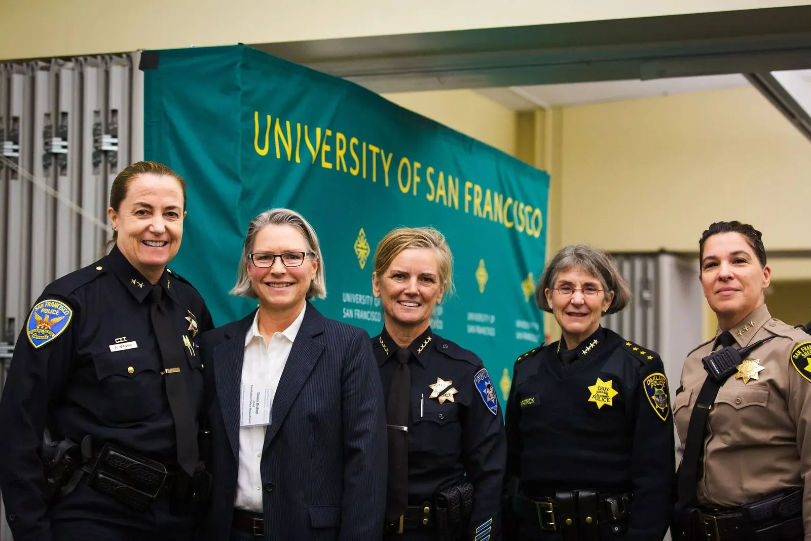 Group of five law enforcement professionals posing in front of a University of San Francisco banner at a symposium, photographed by Marquee Visuals.