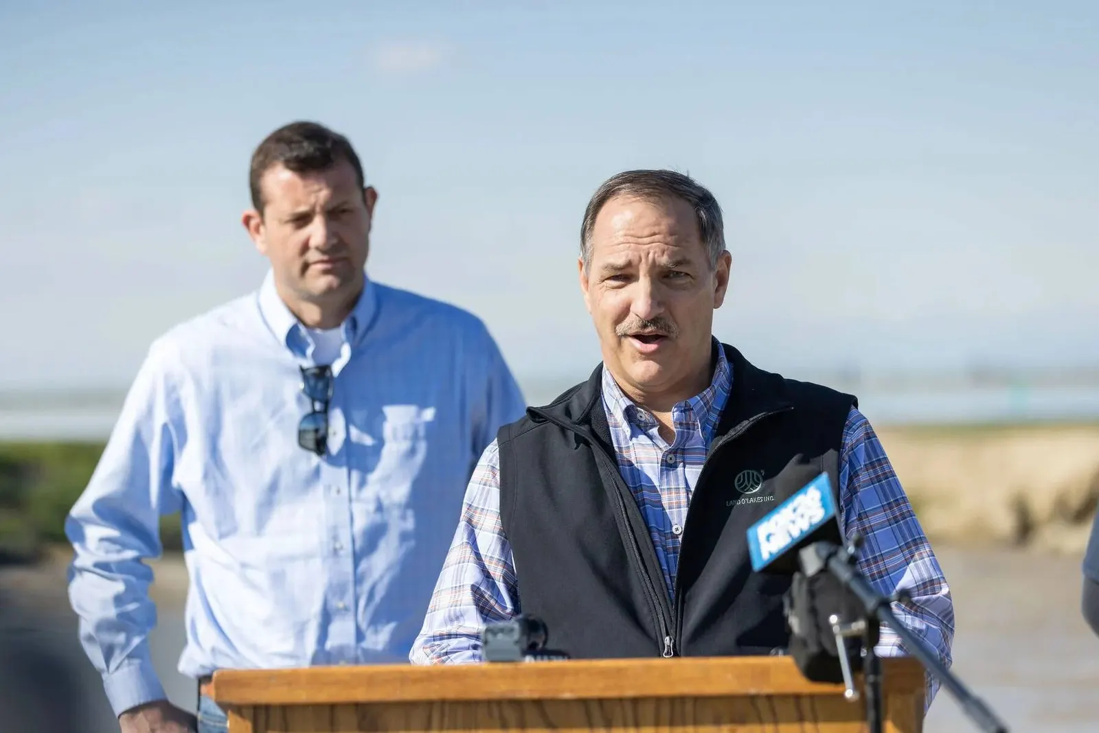 Two men standing near an outdoor podium with microphones at the LOL Hanford event, photographed by Marquee Visuals.