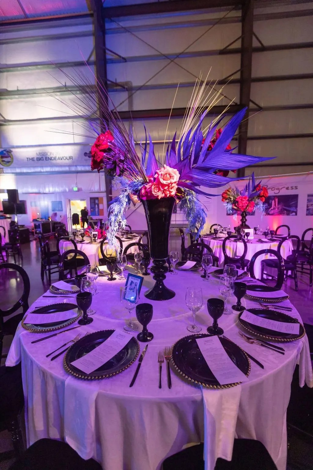 Elegant gala table setting with a tall floral centerpiece under purple lighting at the Nadel University gala, photographed by Marquee Visuals.