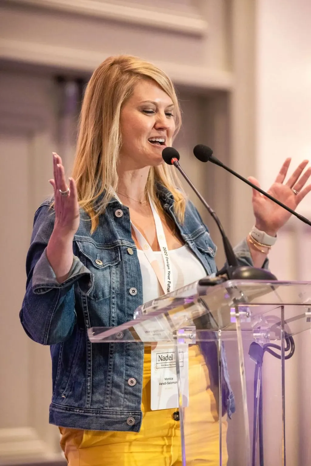 Woman in a denim jacket speaking animatedly at a podium at the Nadel University conference, photographed by Marquee Visuals.