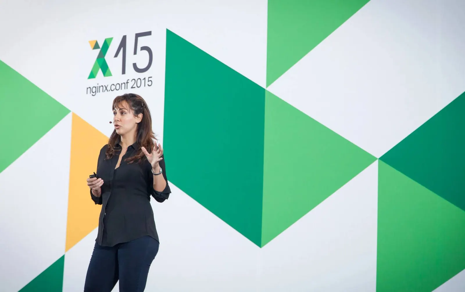 Speaker presenting on stage in front of a green triangle-patterned backdrop at the NGINX conference, photographed by Marquee Visuals in the Bay Area.