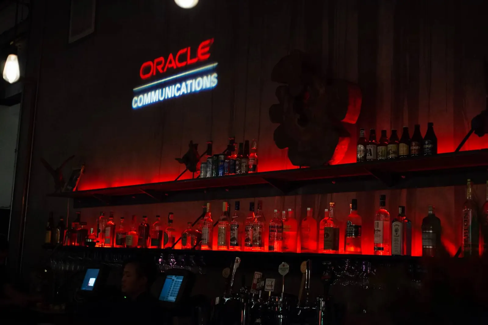 Red-lit bar lounge area with an illuminated Oracle Communications sign at a corporate event, photographed by Marquee Visuals in the Bay Area.