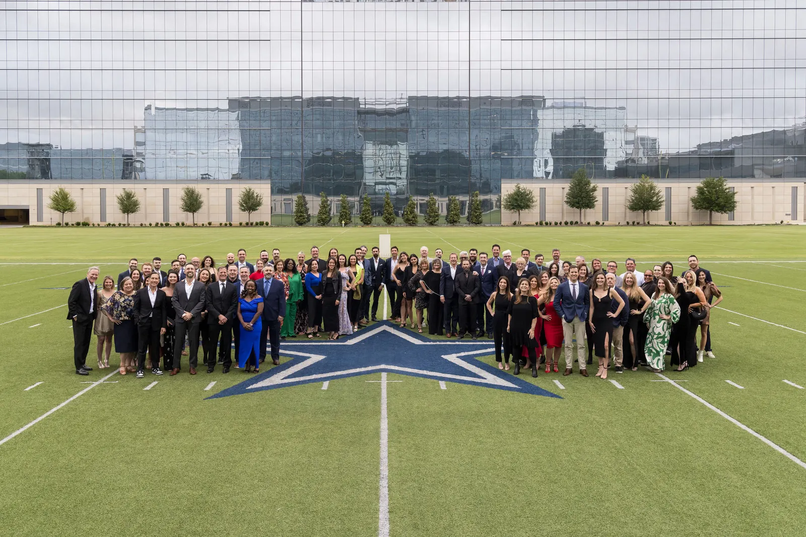 Large formal group photo of attendees on a football field at midfield, photographed by Marquee Visuals.