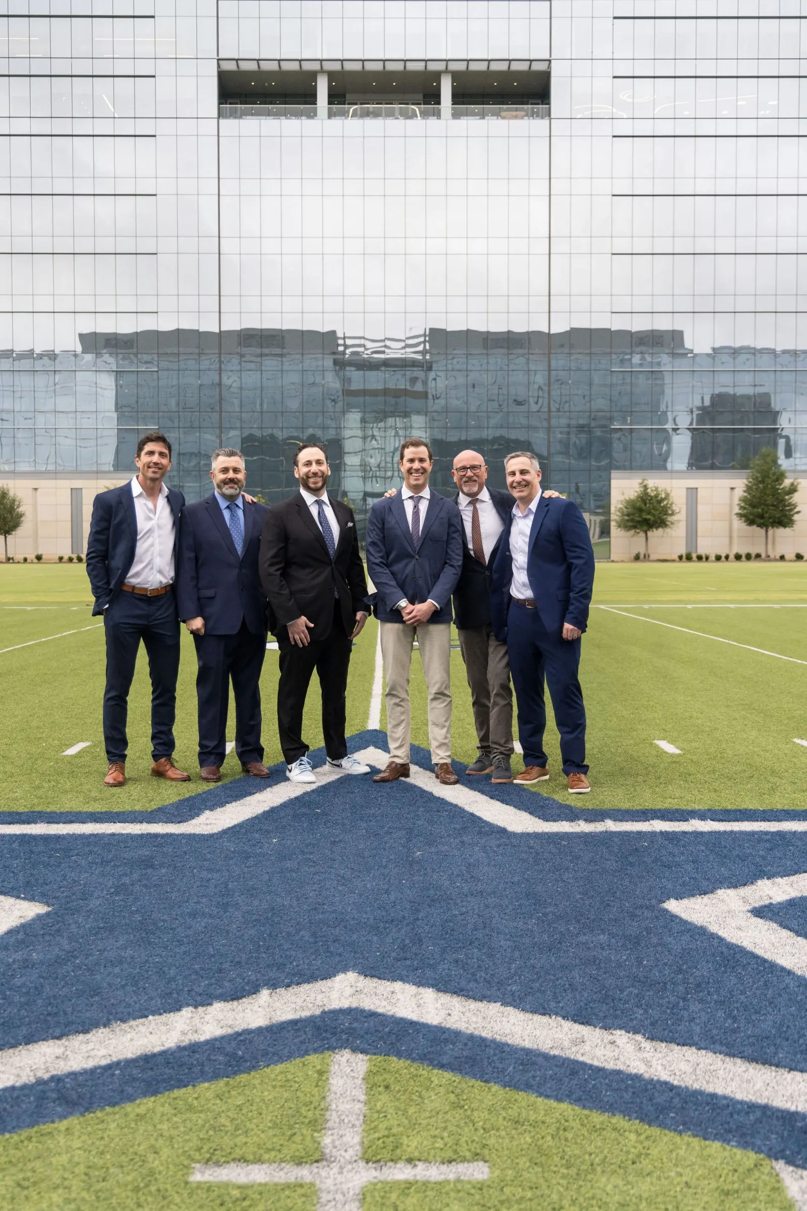 Small group of men in suits standing on a football field near the midfield logo, photographed by Marquee Visuals.