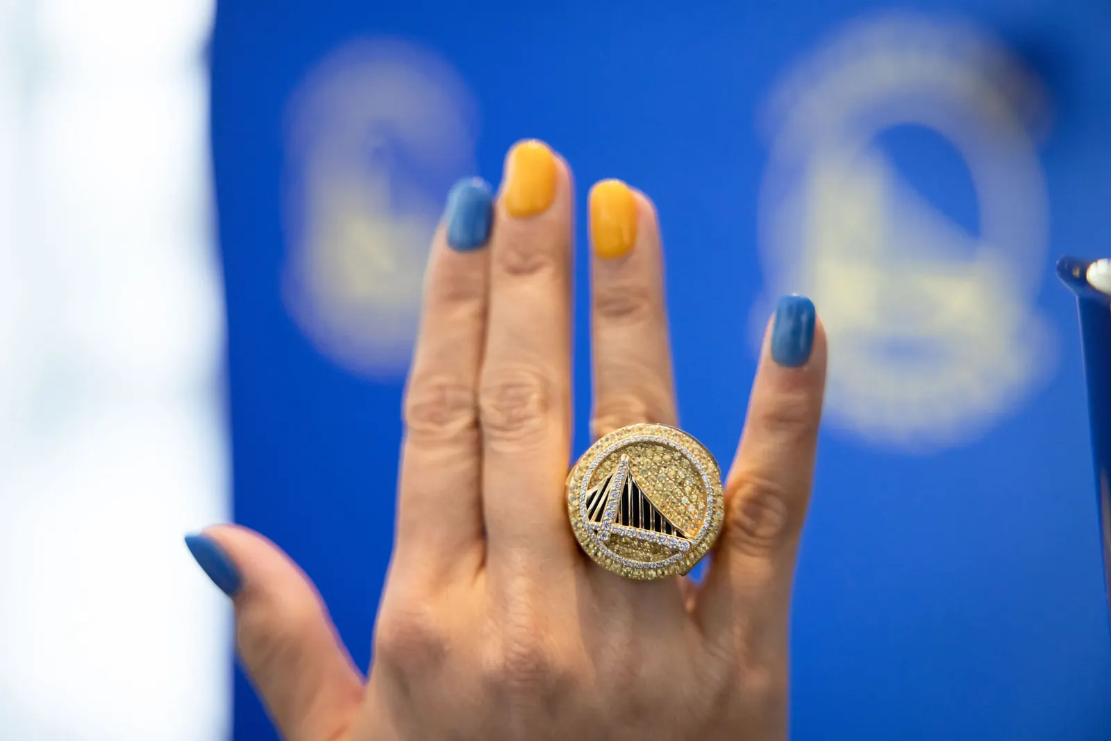 Close-up of a hand with blue nail polish wearing a Golden State Warriors championship ring, photographed by Marquee Visuals.