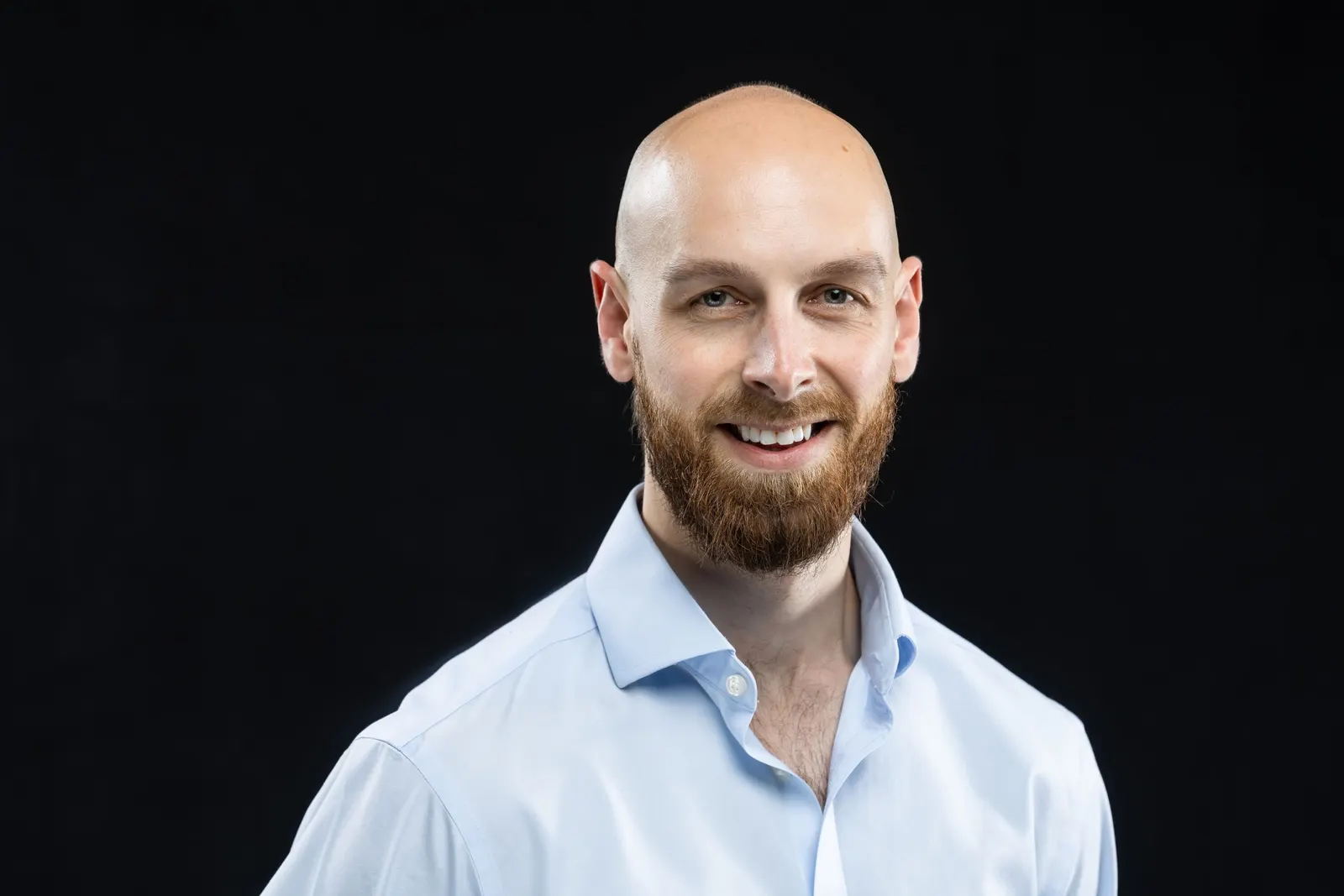 Corporate headshot of a smiling bald man in a light blue button-down shirt on a black studio backdrop, photographed by Marquee Visuals in Los Angeles.