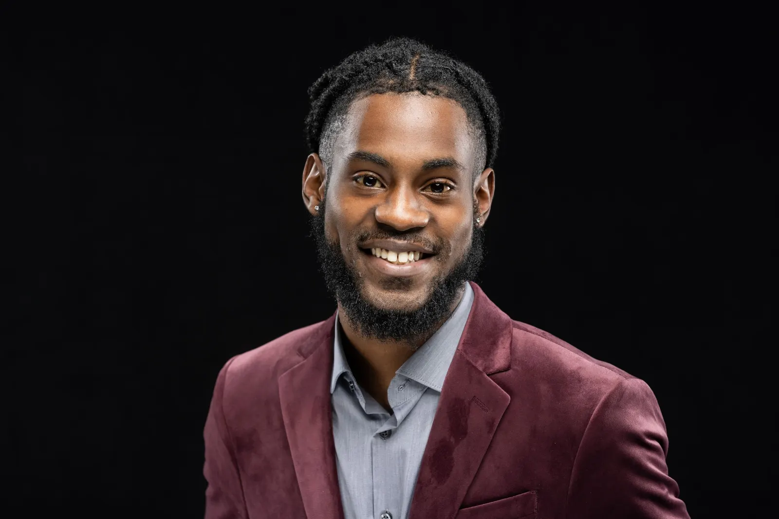 Corporate headshot of a smiling man with a beard in a maroon blazer and gray shirt on a black studio backdrop, photographed by Marquee Visuals in Los Angeles.