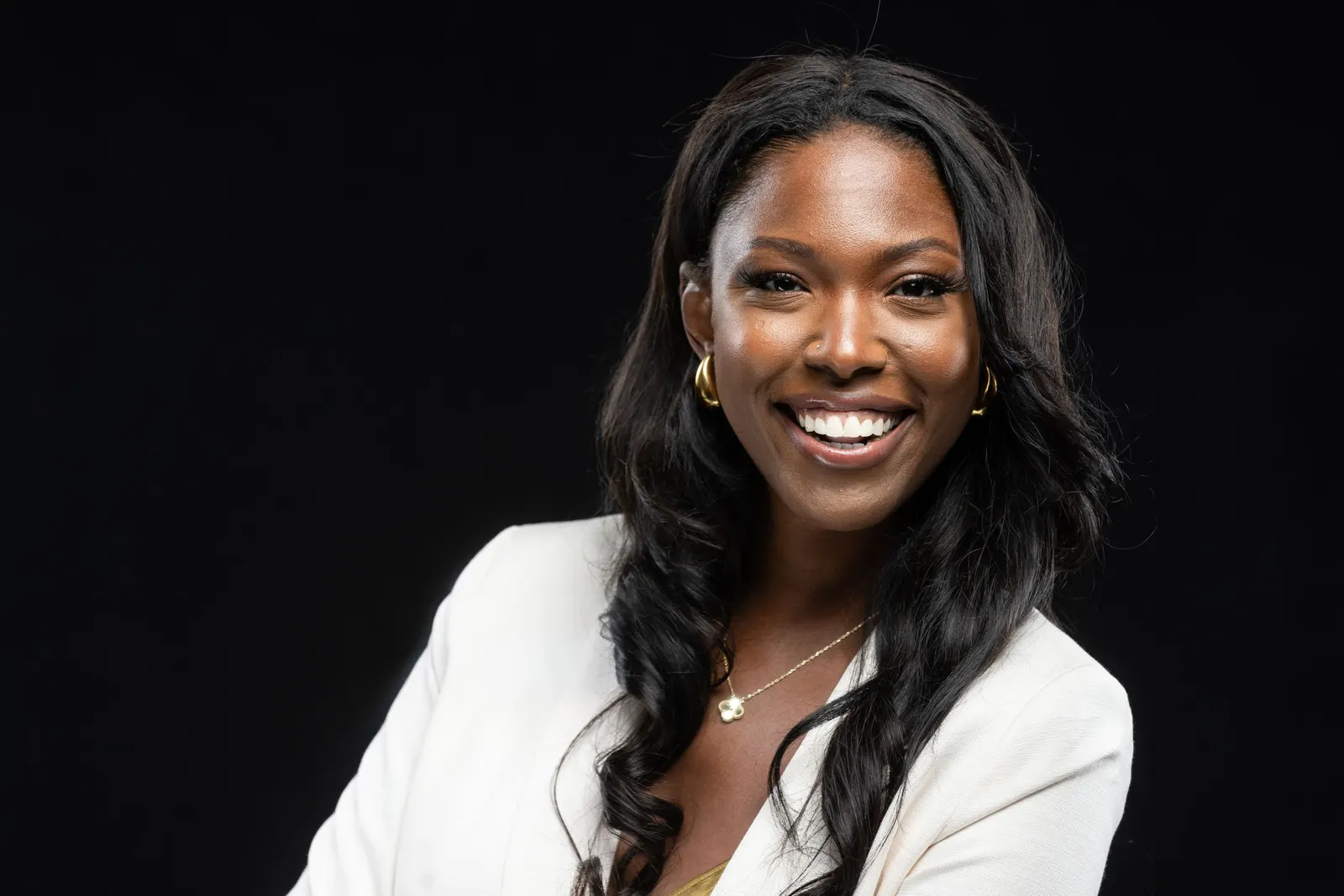 Corporate headshot of a smiling woman with braided hair in a black blazer on a black studio backdrop, photographed by Marquee Visuals in Los Angeles.