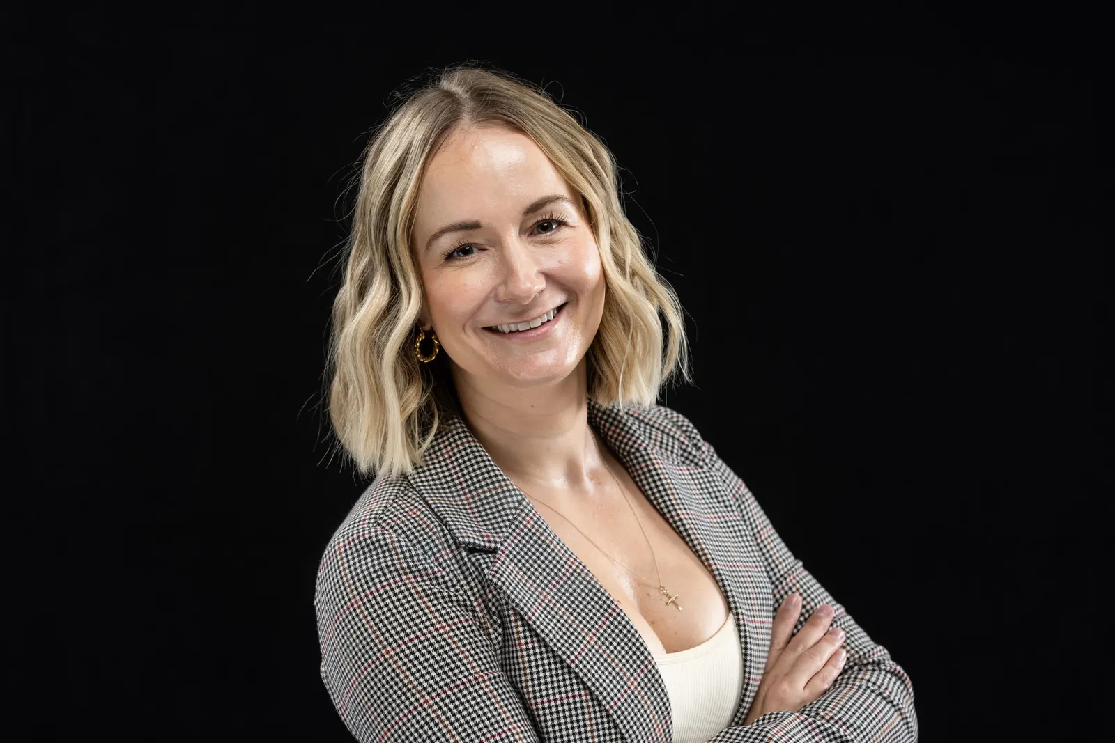 Corporate headshot of a smiling blonde woman in a gray blazer, arms crossed, on a black studio backdrop, by Marquee Visuals in Los Angeles.