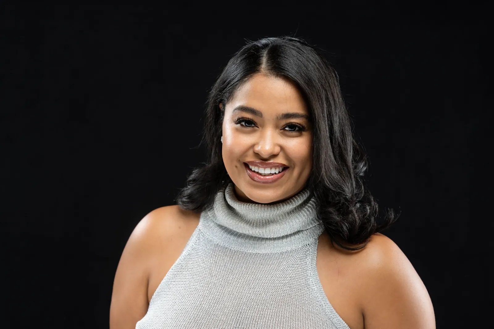 Corporate headshot of a smiling woman in a gray turtleneck sweater on a black studio backdrop, photographed by Marquee Visuals in Los Angeles.