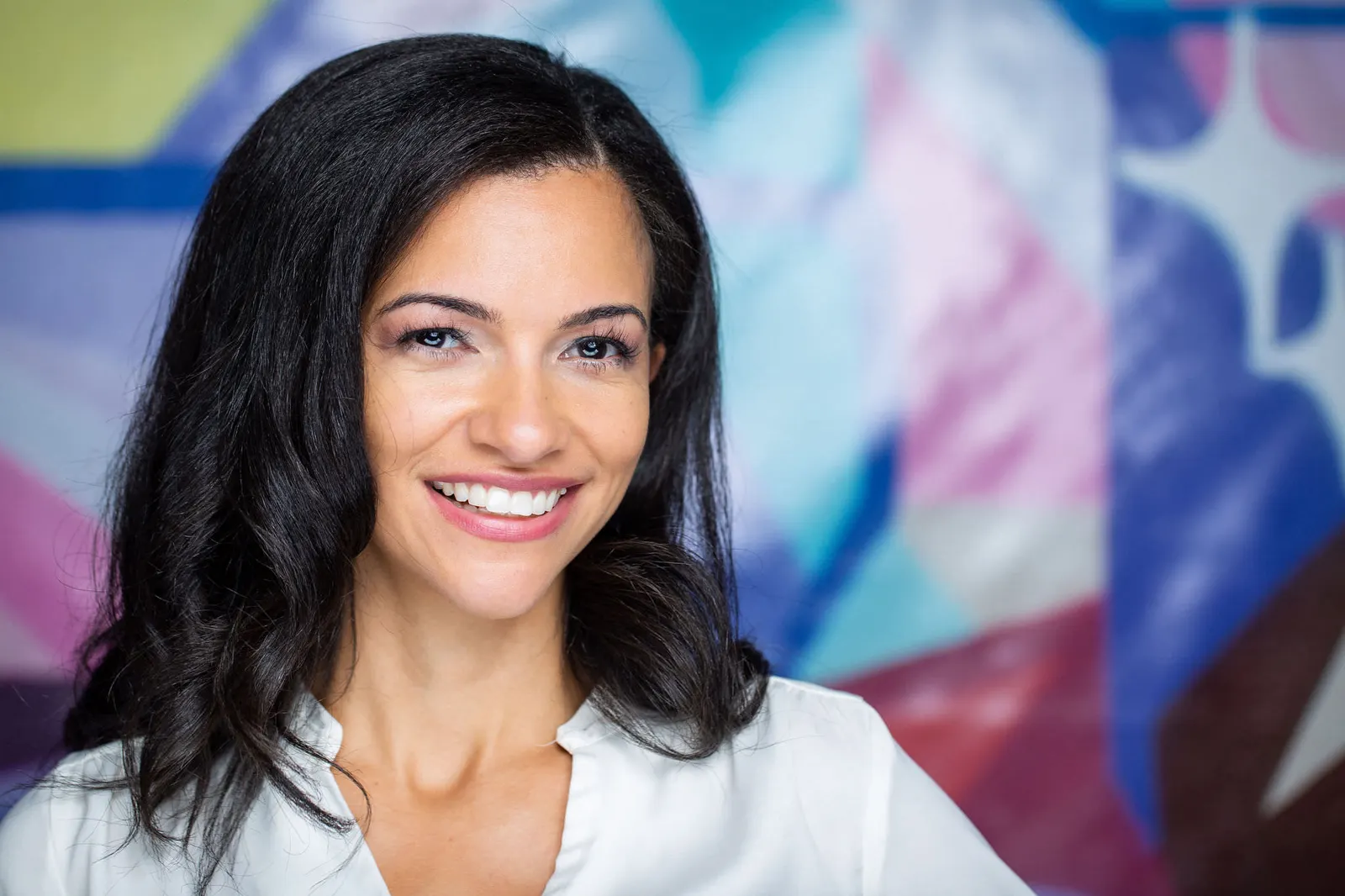 Corporate headshot of a smiling woman in a white blouse against a colorful mural backdrop, photographed by Marquee Visuals in Los Angeles.