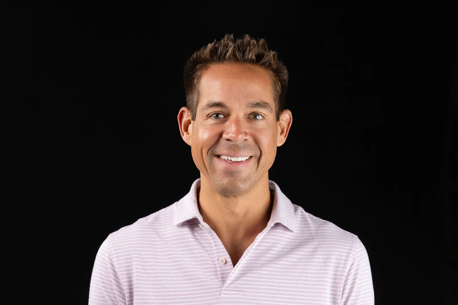 Corporate headshot of a smiling man in a light pink checked shirt on a black studio backdrop, photographed by Marquee Visuals in Los Angeles.