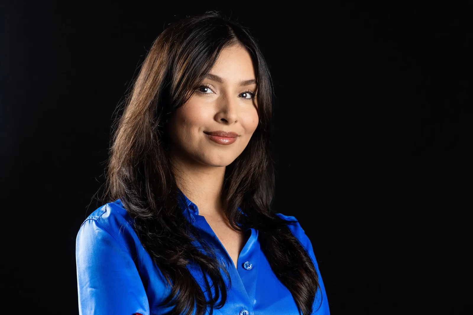 Corporate headshot of a smiling dark-haired woman in a bright blue blouse on a black studio backdrop, photographed by Marquee Visuals in Los Angeles.