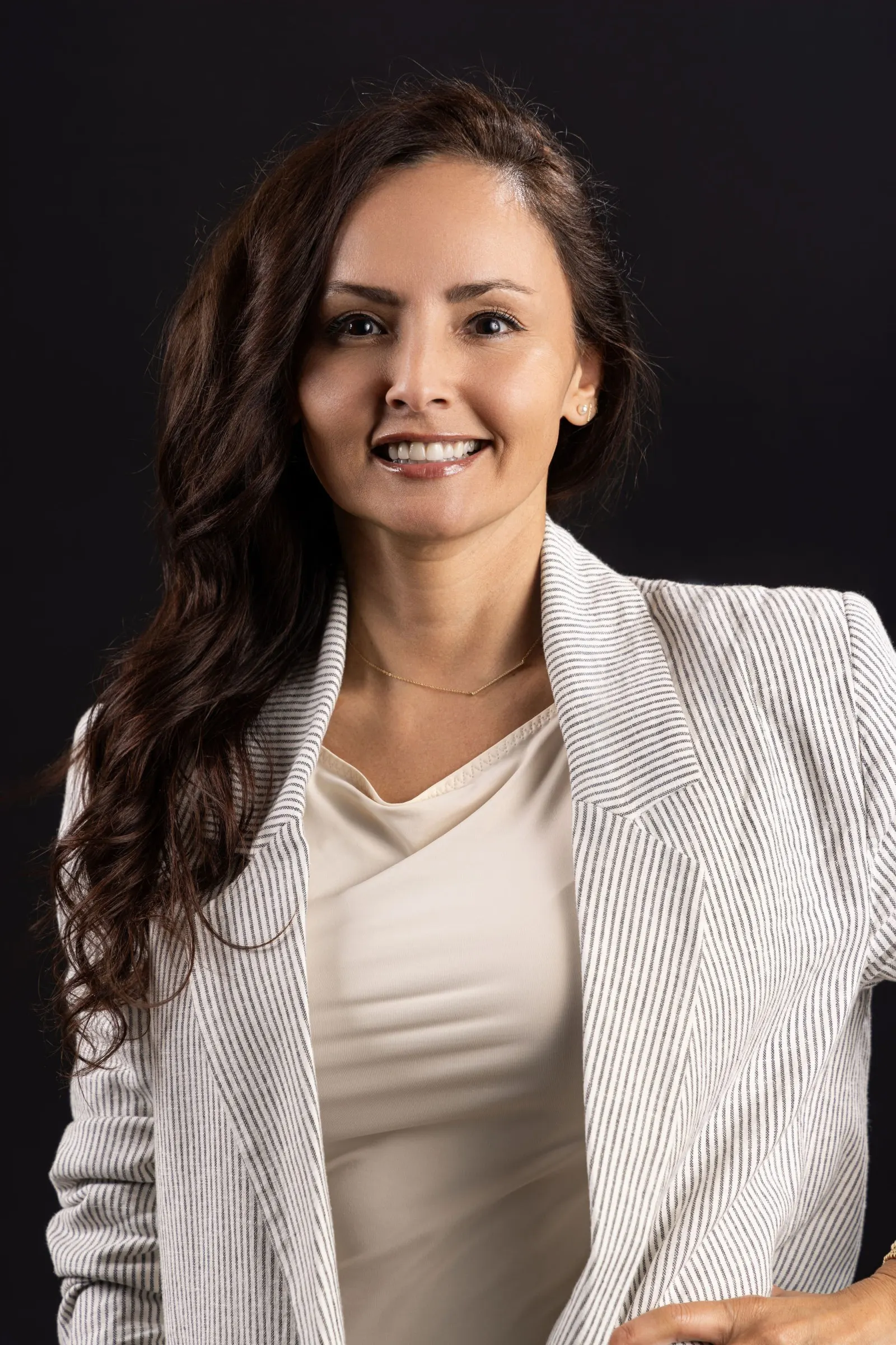 Corporate headshot of a smiling dark-haired woman in a cream cardigan on a black studio backdrop, photographed by Marquee Visuals in Los Angeles.