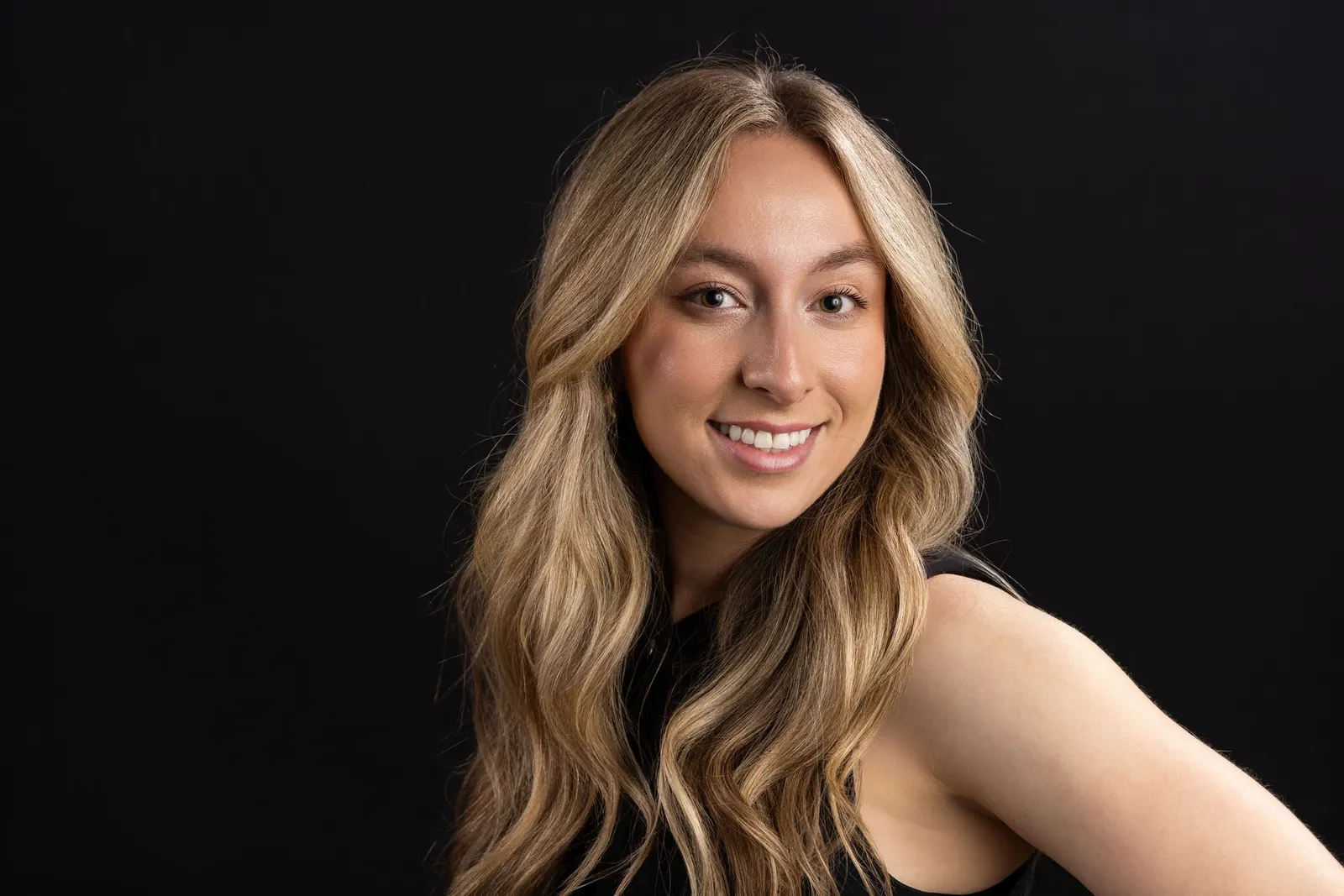 Corporate headshot of a smiling blonde woman in a sleeveless top on a black studio backdrop, photographed by Marquee Visuals in Los Angeles.