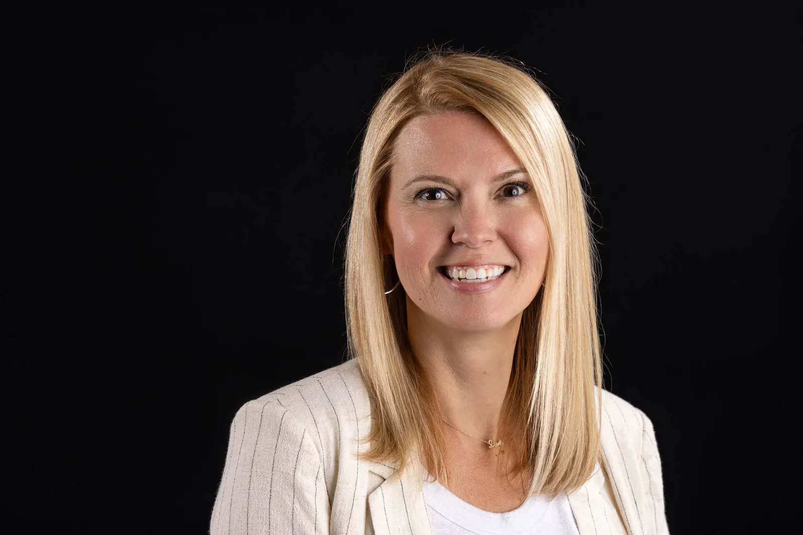 Corporate headshot of a smiling blonde woman in a white cardigan on a black studio backdrop, photographed by Marquee Visuals in Los Angeles.