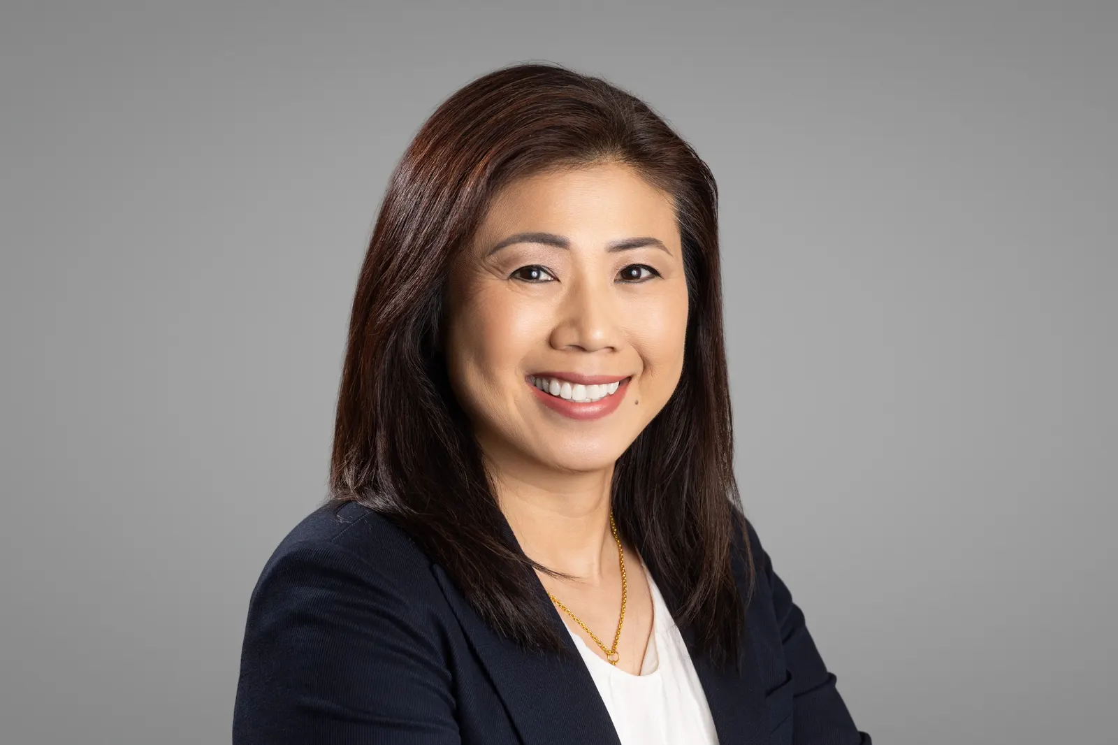 Corporate headshot of a smiling woman in a black blazer and white top on a light gray studio backdrop, photographed by Marquee Visuals in Los Angeles.