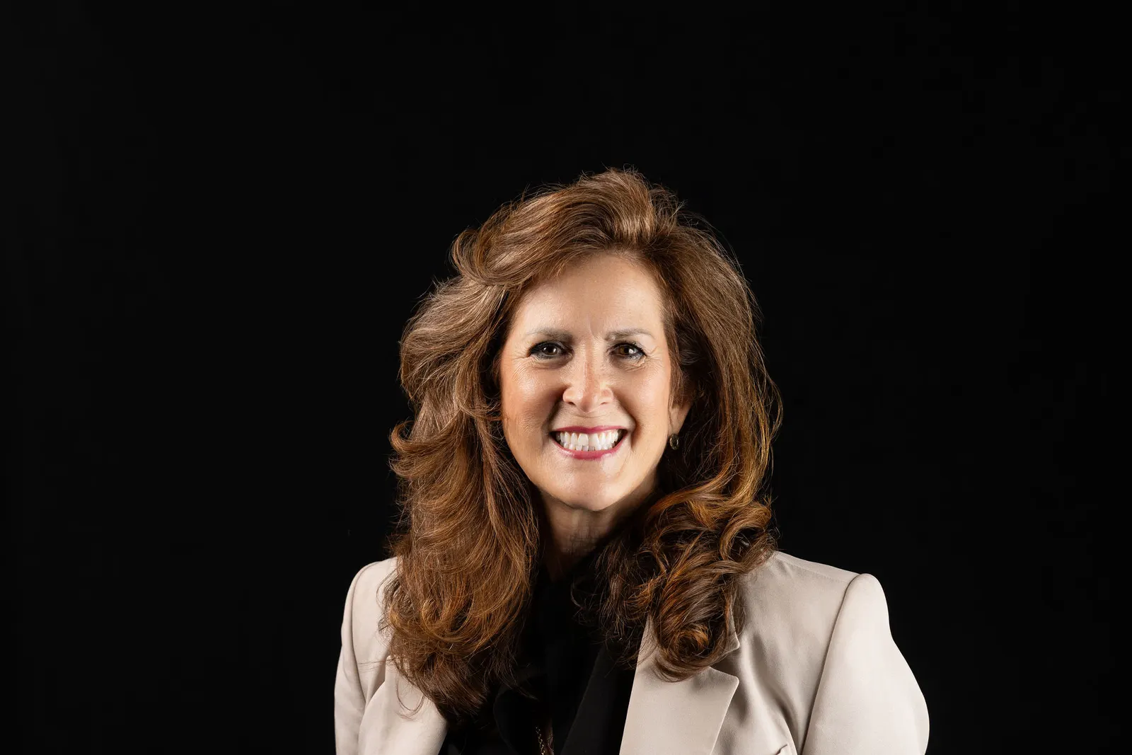 Corporate headshot of a smiling woman with curly hair in a cream blazer on a black studio backdrop, photographed by Marquee Visuals in Los Angeles.