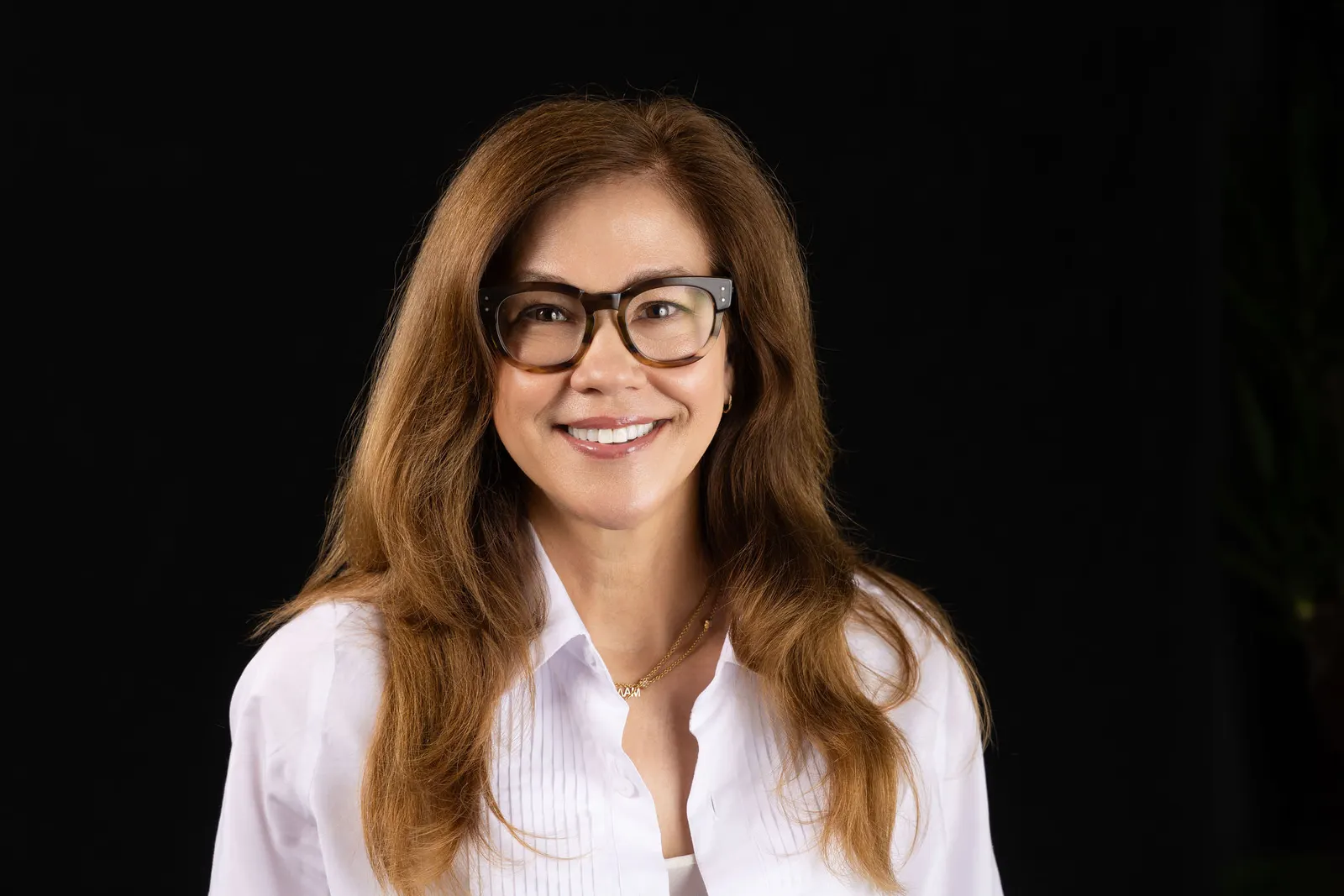 Corporate headshot of a smiling woman wearing glasses and a white blouse on a black studio backdrop, photographed by Marquee Visuals in Los Angeles.