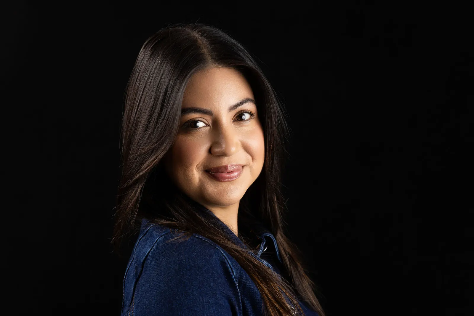 Corporate headshot of a smiling woman in a navy top photographed at a slight profile angle on a black backdrop, by Marquee Visuals in Los Angeles.