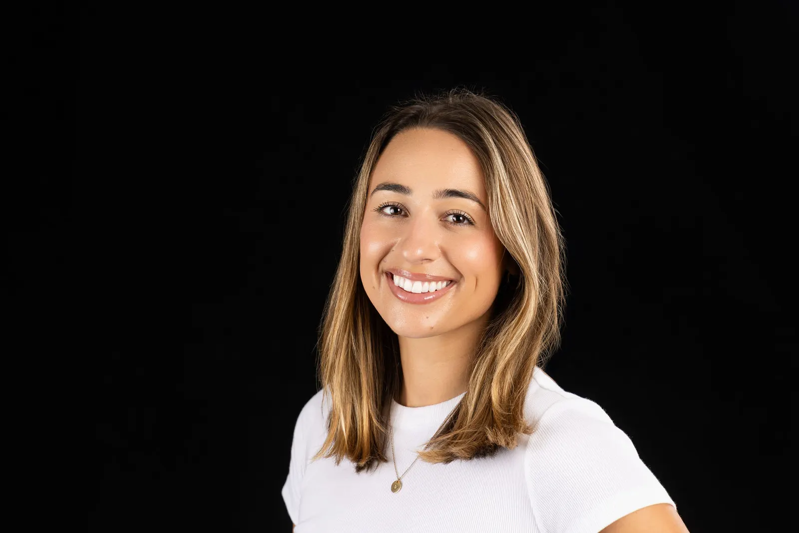 Corporate headshot of a smiling woman with wavy hair in a white top on a black studio backdrop, photographed by Marquee Visuals in Los Angeles.