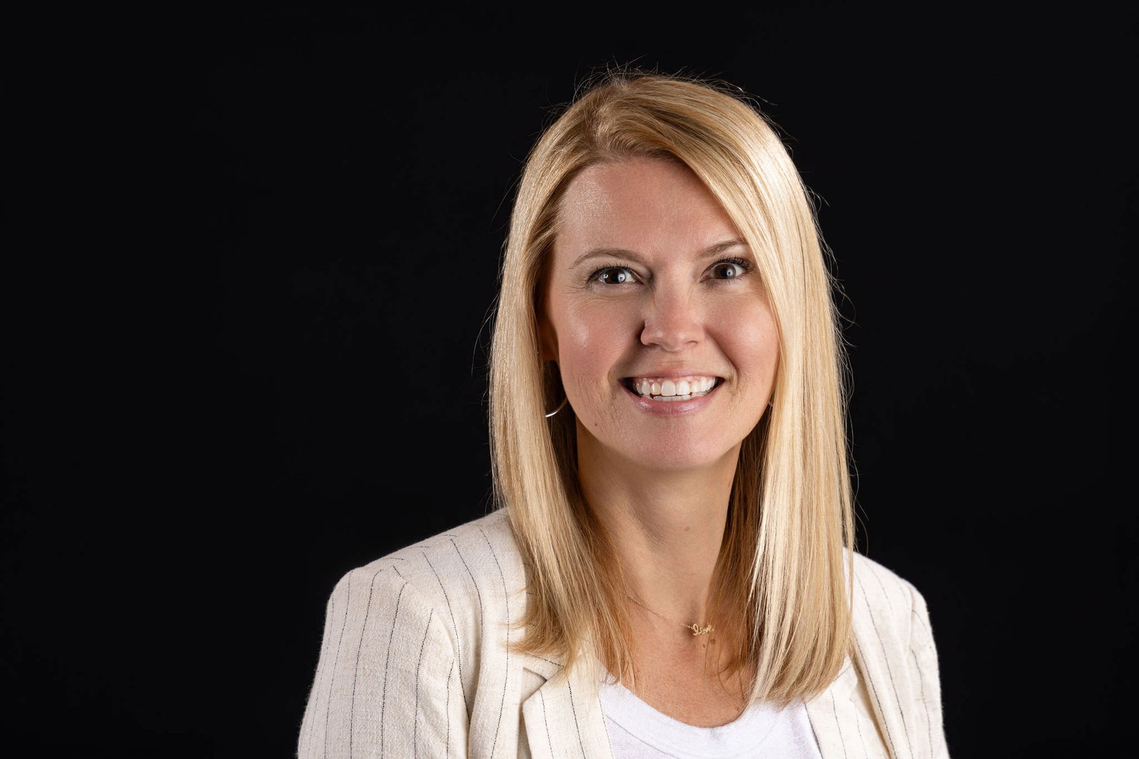 Corporate headshot of a smiling blonde woman in a white cardigan on a black studio backdrop, photographed by Marquee Visuals in Los Angeles.
